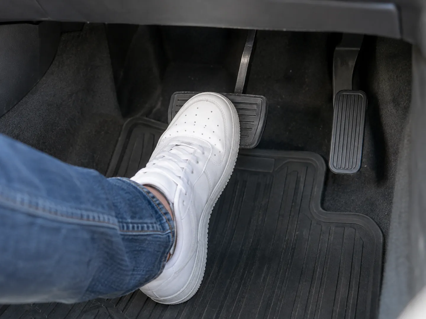 A low view of a car footwell with just two pedals, a driver's trainer resting on the wide brake pedal