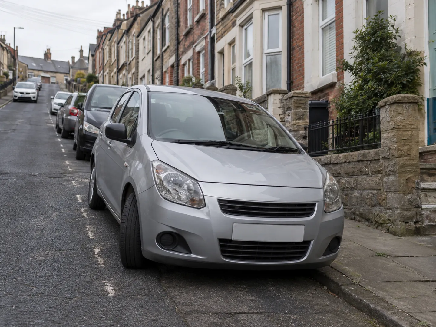 A small hatchback parked close to the kerb on a steep residential street, front wheel turned in towards the kerb