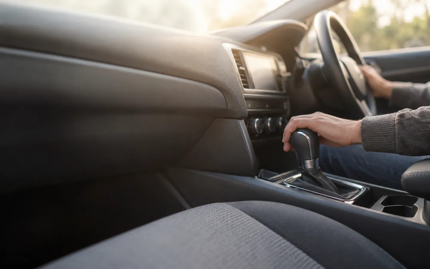 A hand resting on an automatic gear selector set to P in a modern car interior, soft daylight through the windscreen